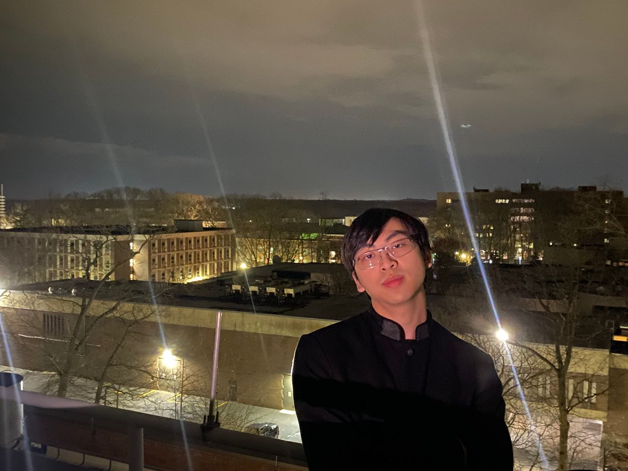 James Leung on a rooftop at night, above brick buildings and bright streetlights.