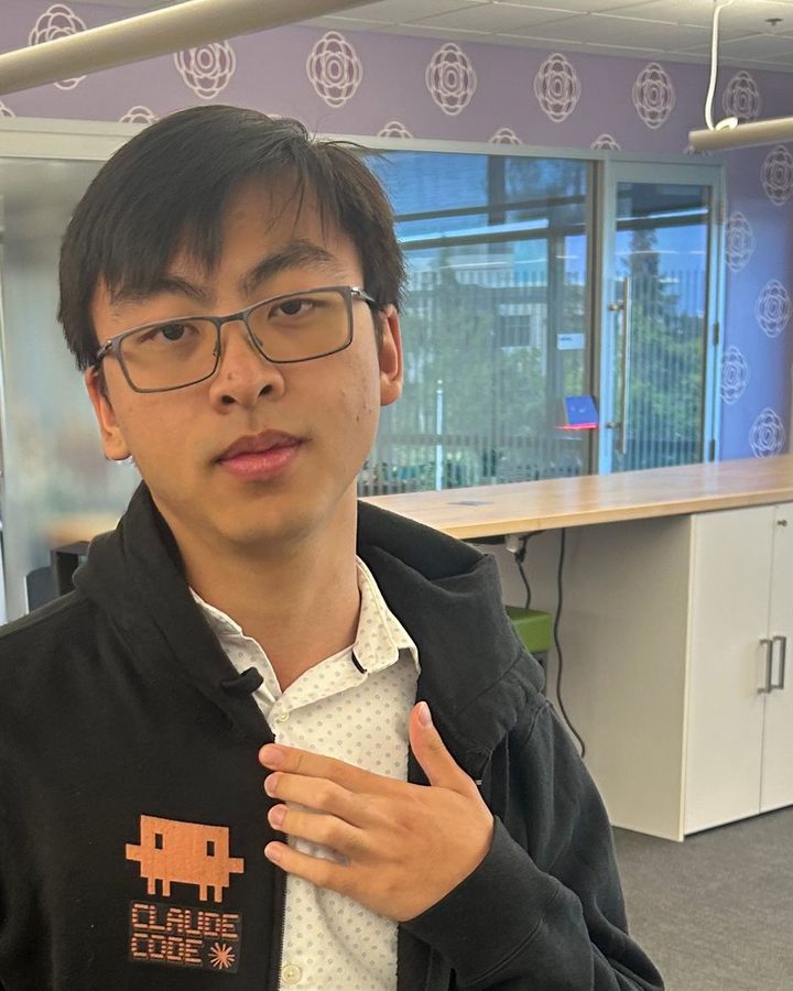 James Leung in an office, wearing a black Claude Code hoodie over a white shirt.