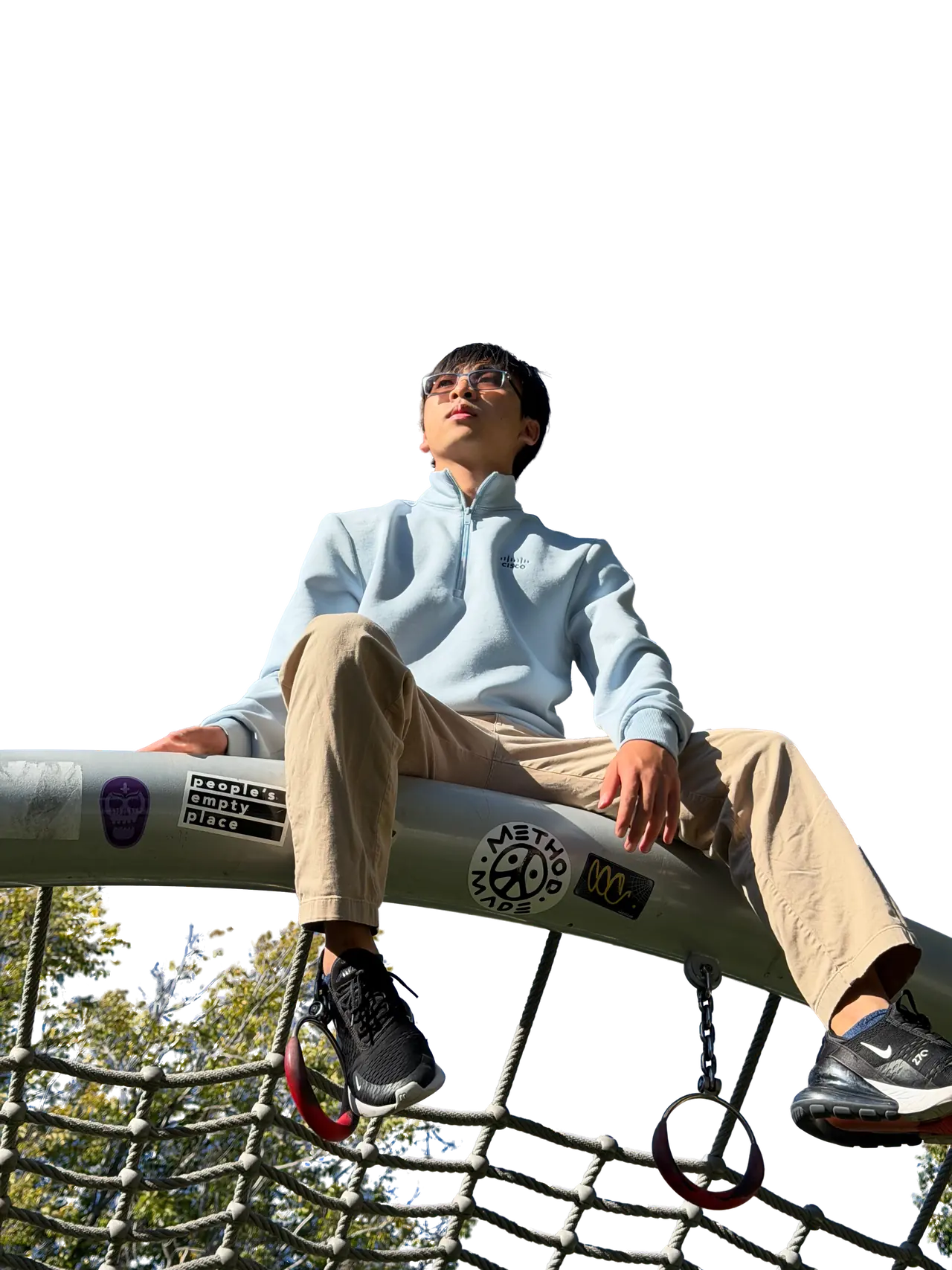 James Leung sits on the top rail of a playground climbing frame, looking up.
